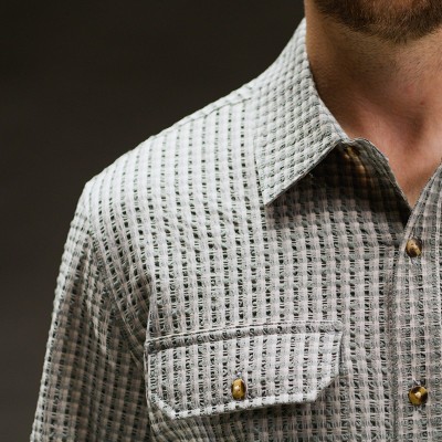 Close-up of a textured green check button-down shirt collar and chest pocket with brass snaps.