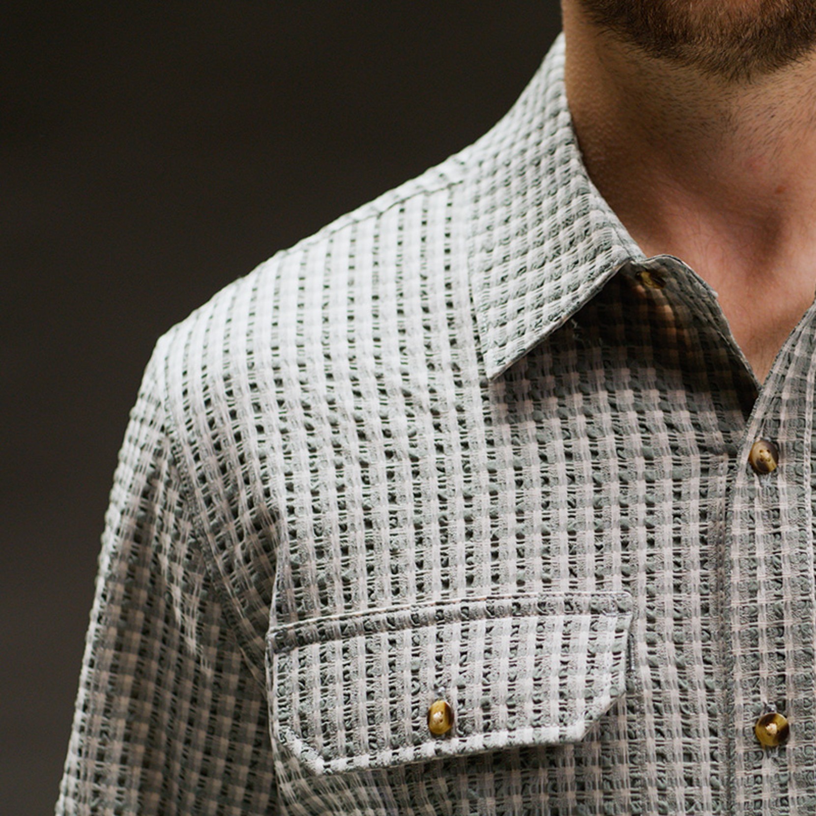 Close-up of a textured green check button-down shirt collar and chest pocket with brass snaps.