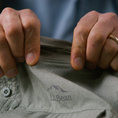 Hands stretching olive fabric to show flexibility with an L L ean logo printed inside the garment.