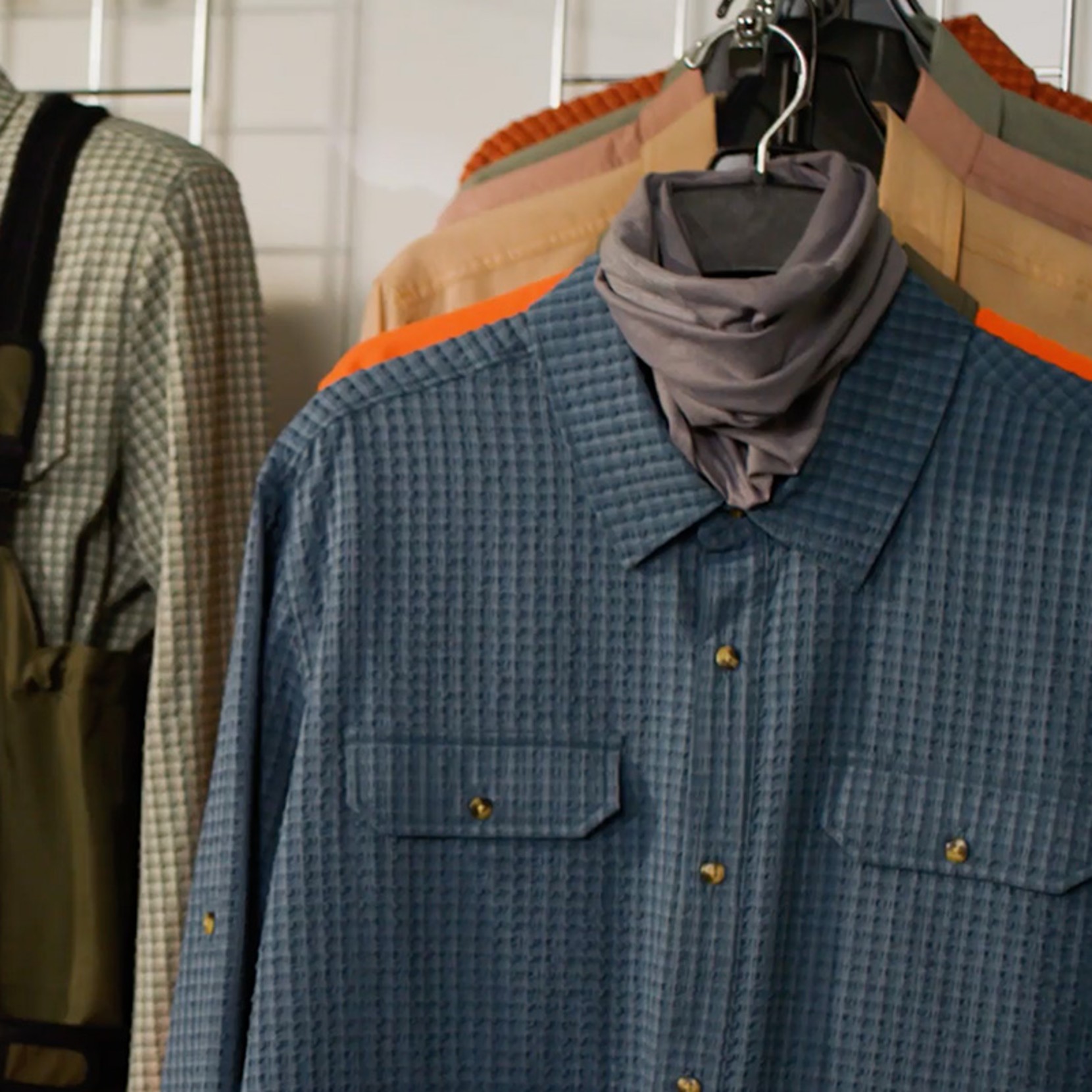 Blue check button-down shirt hanging on a rack with other shirts layered behind it.
