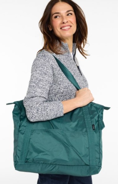 Smiling woman carries a large teal color tote bag while wearing a gray knit pullover.