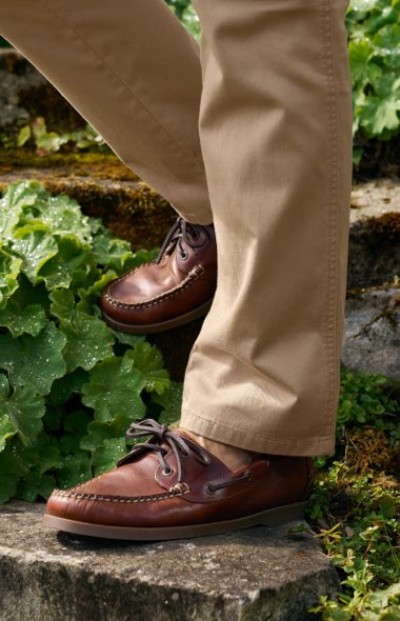 Close up image of person in brown leather moccasins and khaki pants on stone steps surrounded by green foliage.