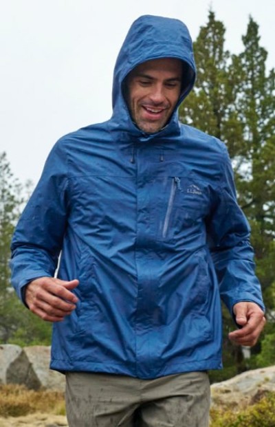 Person wearing a blue hooded rain jacket walks outdoors on a wet, overcast day.