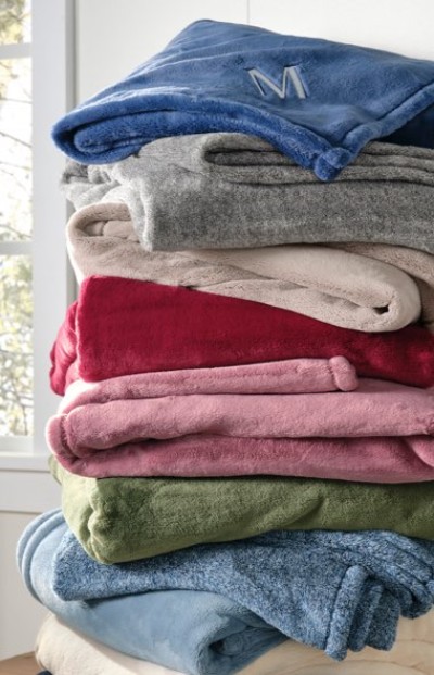 A tall stack of soft, folded blankets in various colors, including blue, gray, red, pink, green, and beige.