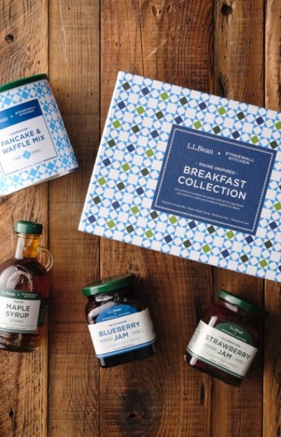 Breakfast gift set displayed on a wooden surface includes pancake mix, maple syrup, blueberry and strawberry jam.