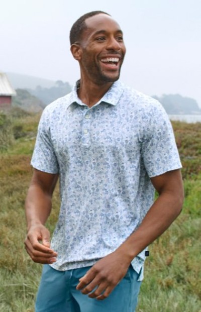 Person wearing a light patterned polo shirt and blue shorts while standing outdoors in a grassy landscape.