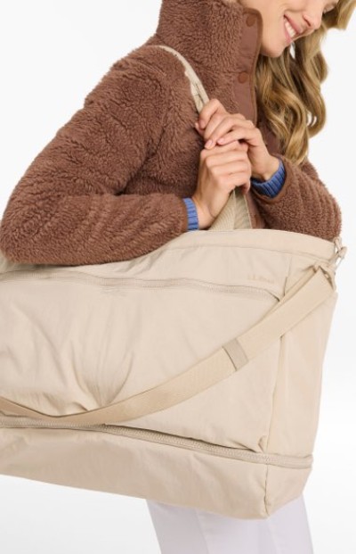 Beige weekender bag carried over the shoulder by someone wearing a textured brown fleece jacket.