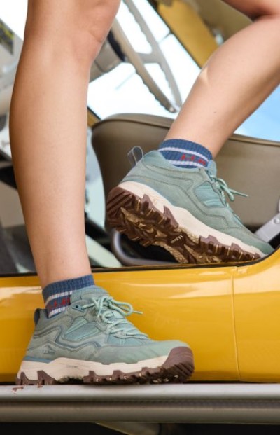 Light hiking shoes with thick treads stepping onto a yellow vehicle’s side in an outdoor setting.