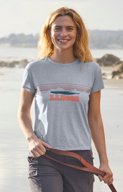 Person wearing a gray graphic T-shirt outdoors near a beach setting.