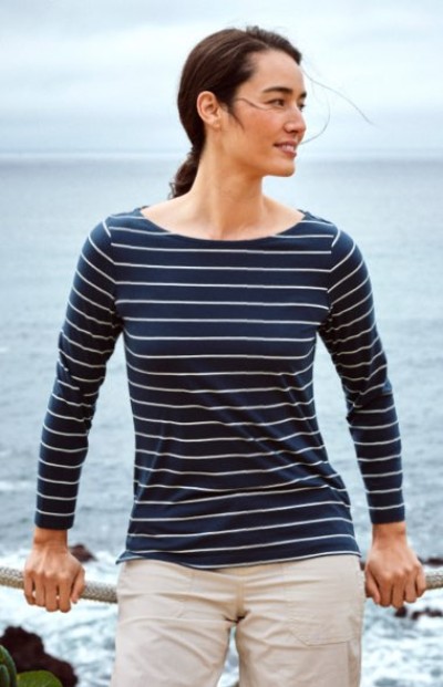 Person in a navy striped shirt and white pants standing near a coastal shoreline.