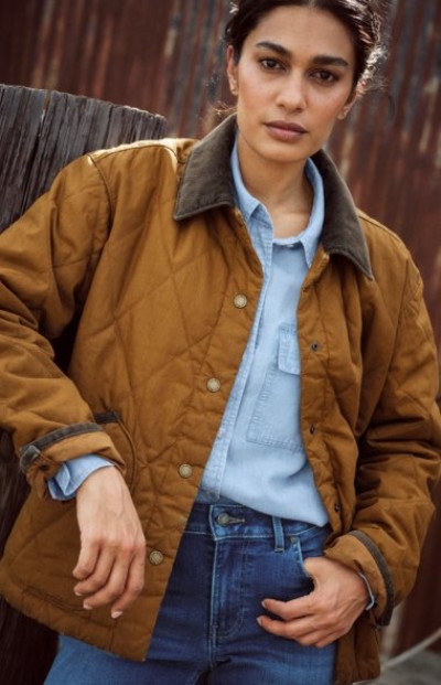 Person wearing a brown jacket layered over a denim shirt in a rustic setting.