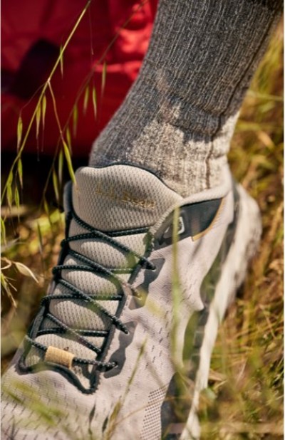 Trail shoe with wool socks stepping through grass on an outdoor path.