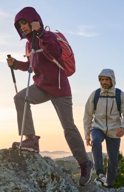 Hiker using trekking poles on a rocky trail with mountain landscape behind.