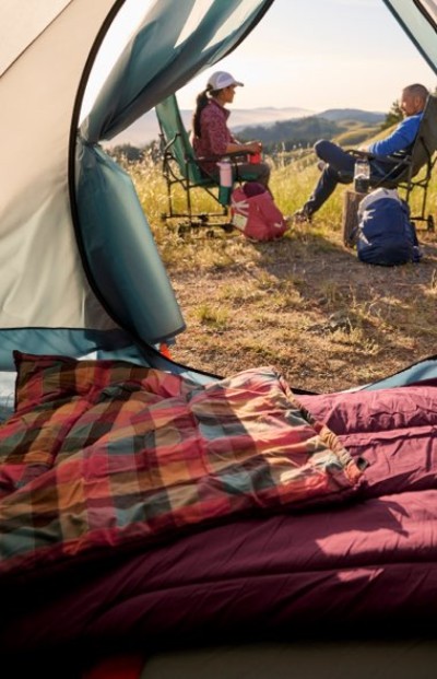 View from inside a cozy tent toward campers seated in chairs with a scenic mountain landscape in the distance.