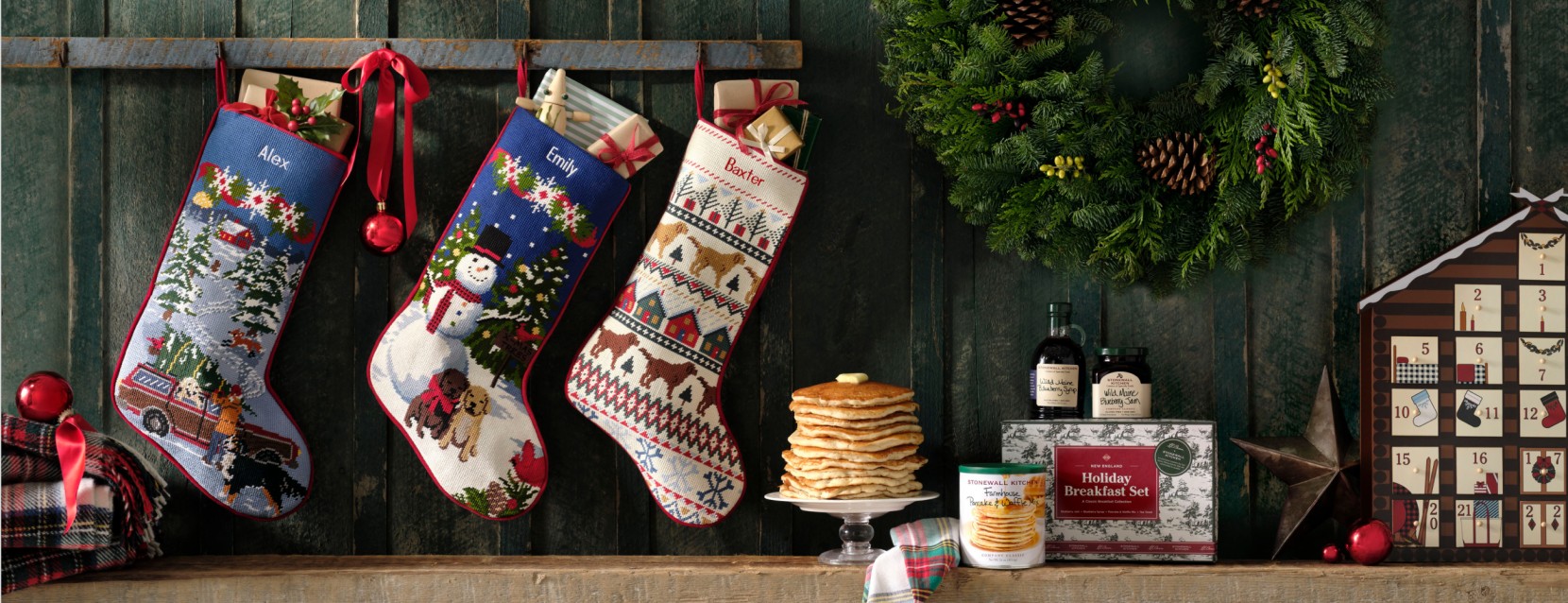 Personalized Christmas stockings hang above a mantel with gifts, wreath, pancakes, and an advent calendar.