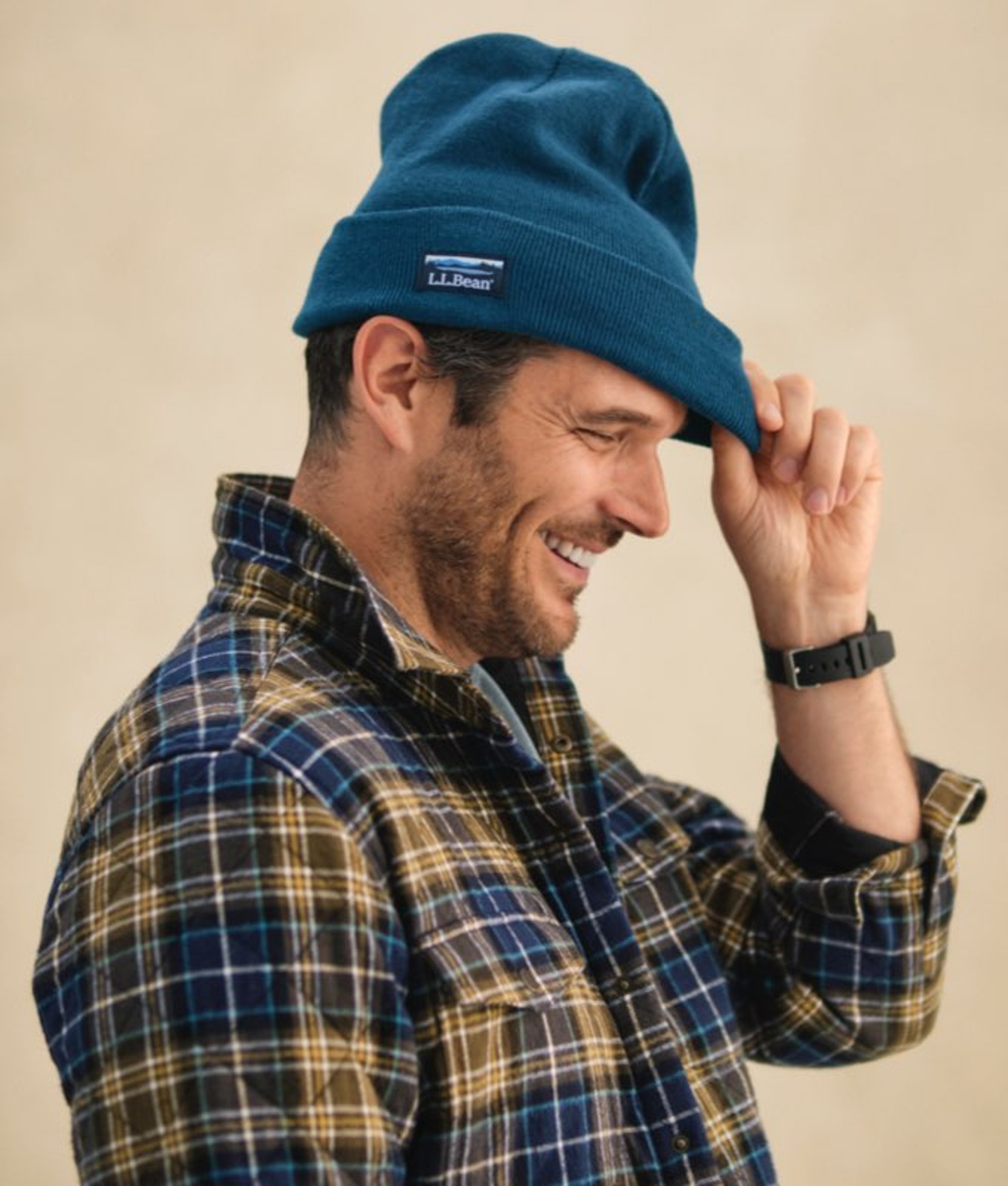 Man adjusting a blue cap while wearing a plaid shirt.