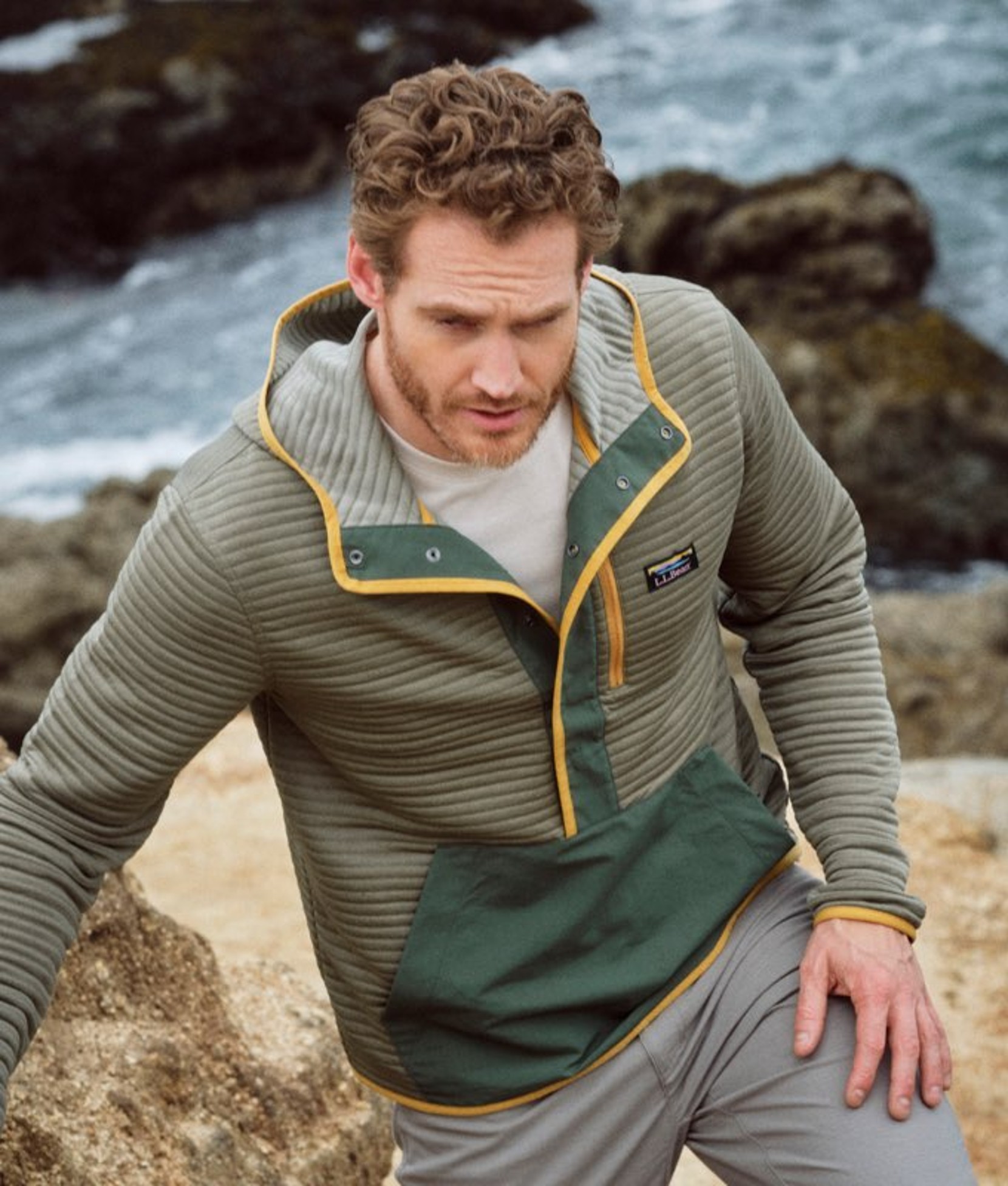 Waist up view of a man stepping on coastal rocks wearing green pullover and shorts.