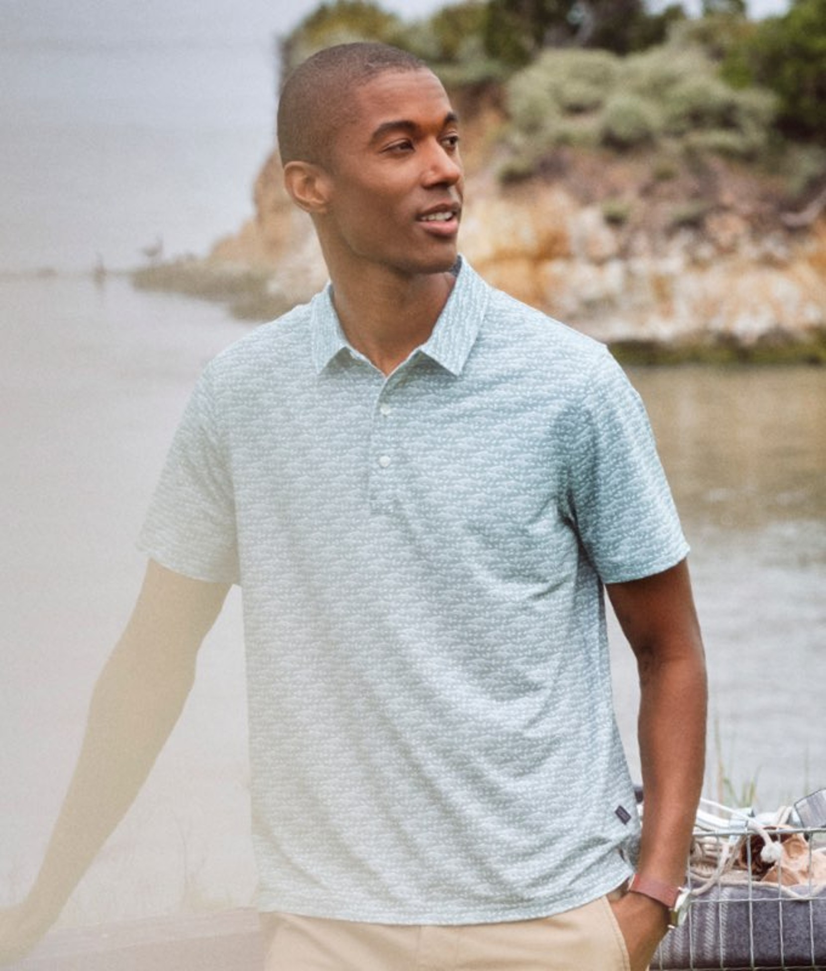 Man in light blue polo shirt standing near shoreline looking off to the side. 