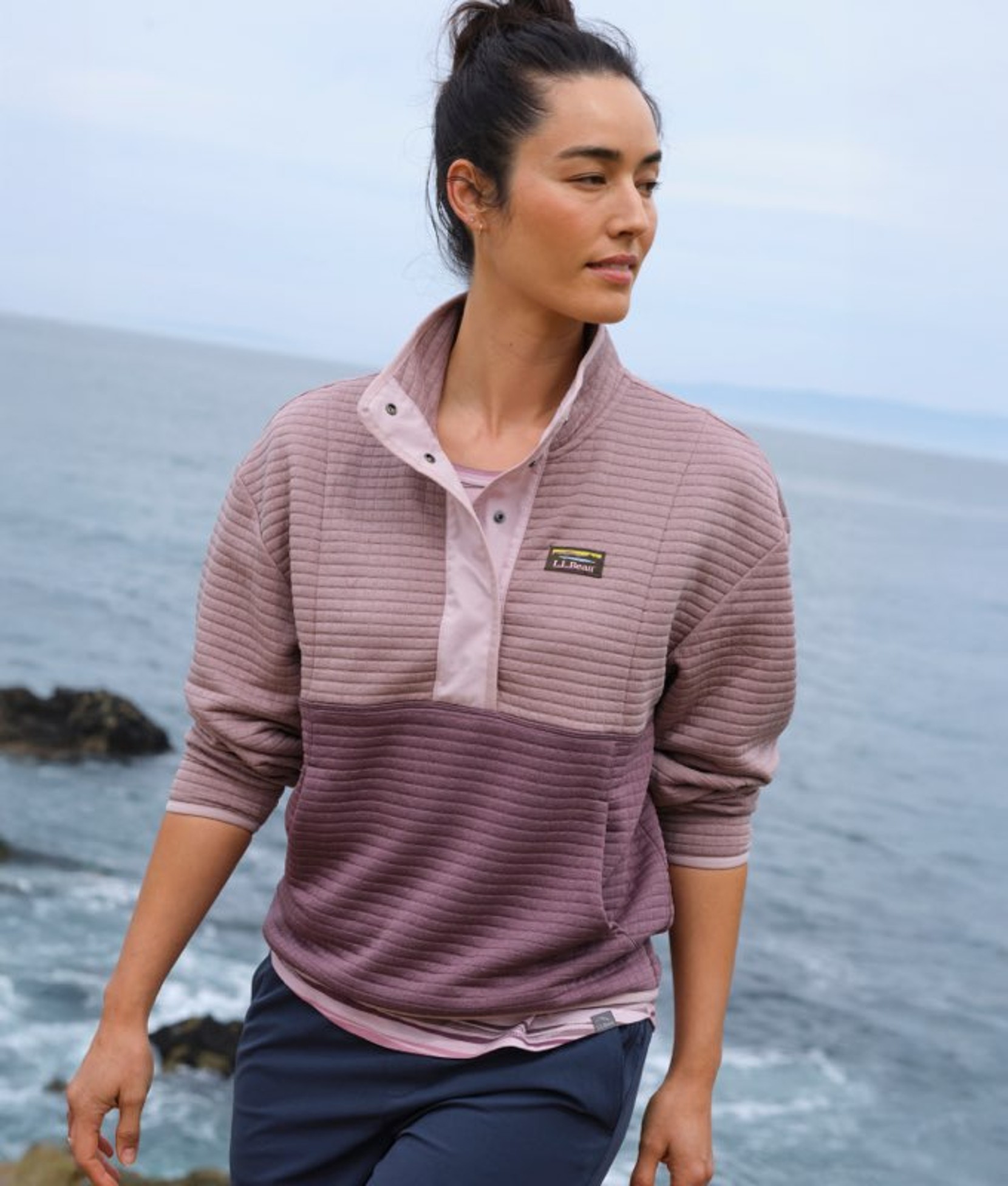 Woman in lavender althletic pullover near coastline misty blue skies.