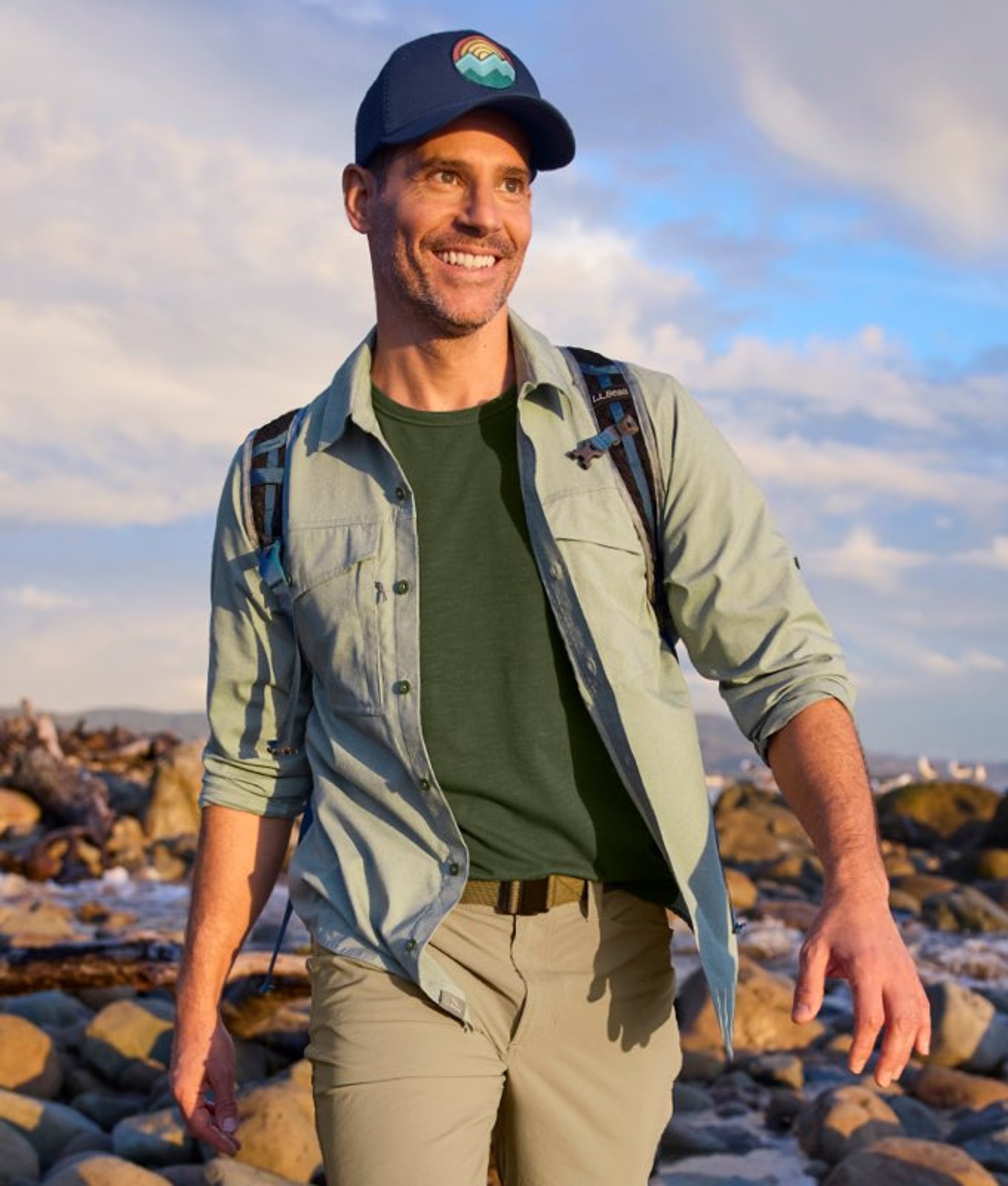 Person wearing a jacket and cap in a rugged outdoor setting with rocks and open sky.