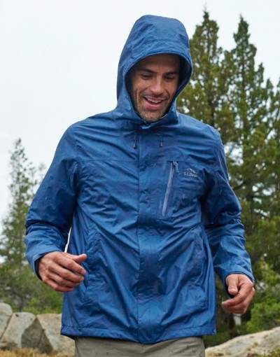 Person in a blue rain jacket walking on a rocky trail in the rain.
