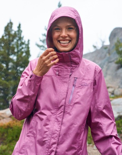 Person in a pink rain jacket standing outdoors among rocks and trees.