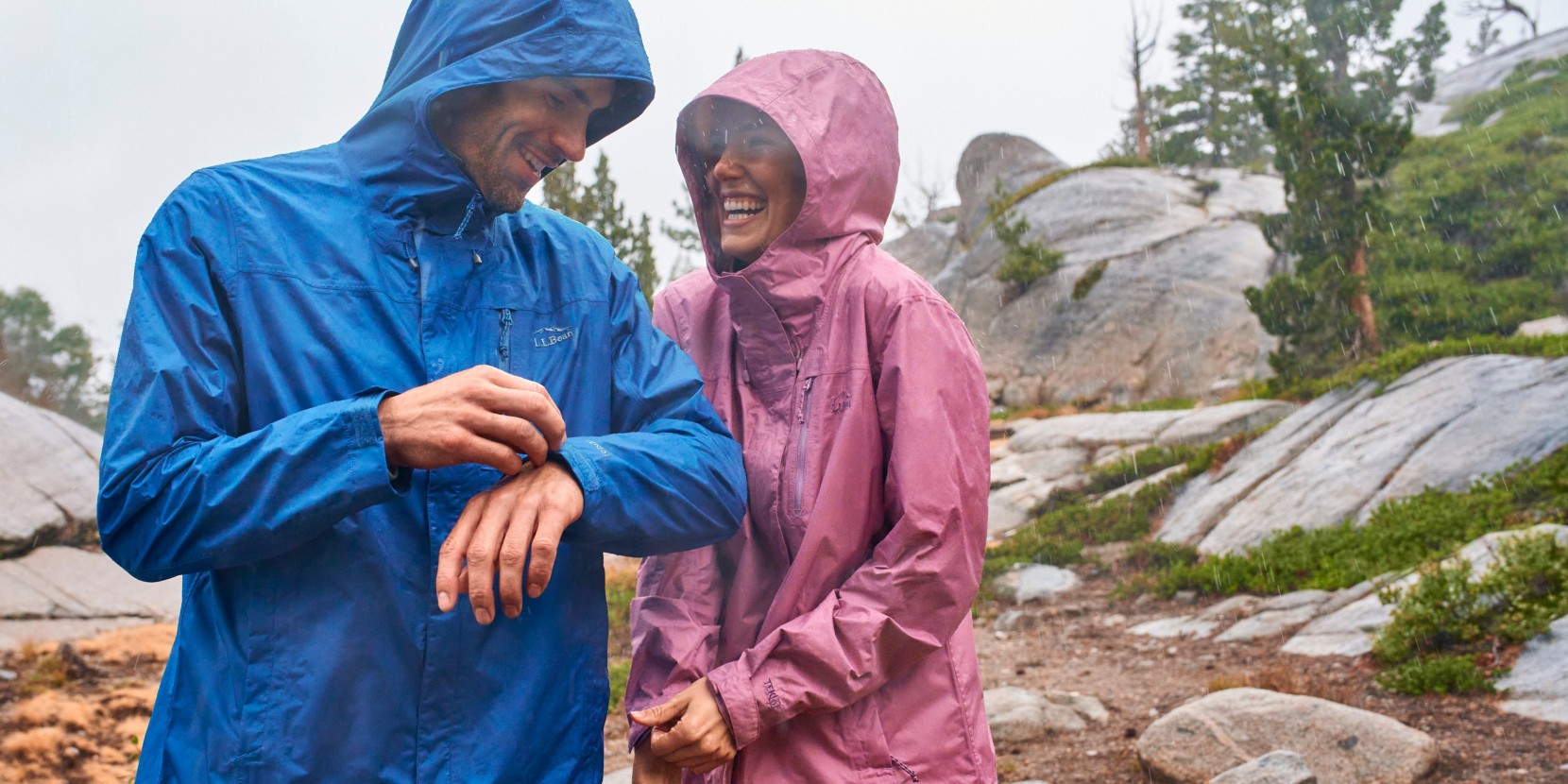 Two people in rain jackets standing on a rocky trail in the rain.