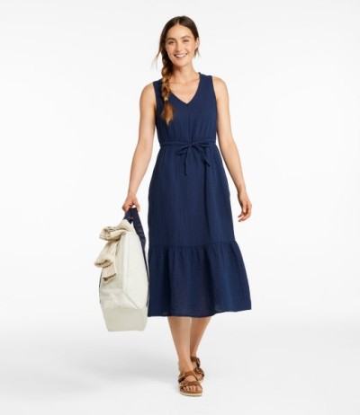 Person in navy sleeveless midi dress holding a tote bag, standing against a light background. 