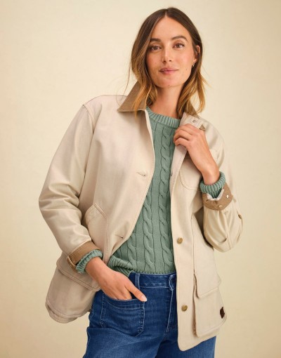 Person wearing a tan field coat over a textured green knit sweater paired with denim jeans in a casual pose.
