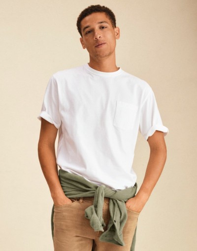Person wearing a white pocket tee paired with tan pants and a green sweatshirt tied at the waist.