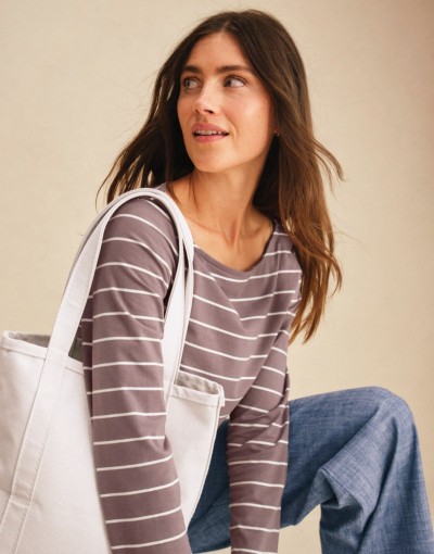 Person wearing a striped long-sleeve top with a light tote bag and relaxed blue pants.
