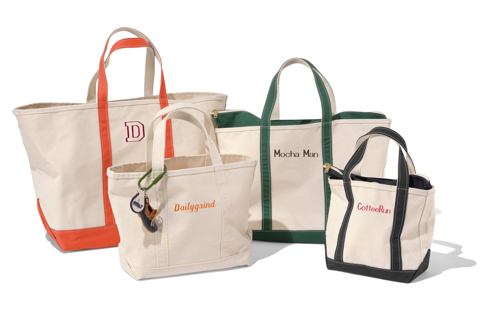 Studio image of four canvas tote bags in various colors with monograms on their fronts.