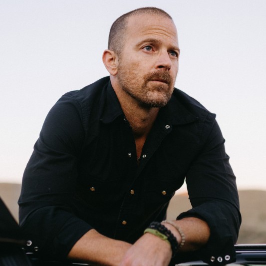 Kip Moore, leaning on a convertible car door, top is down.