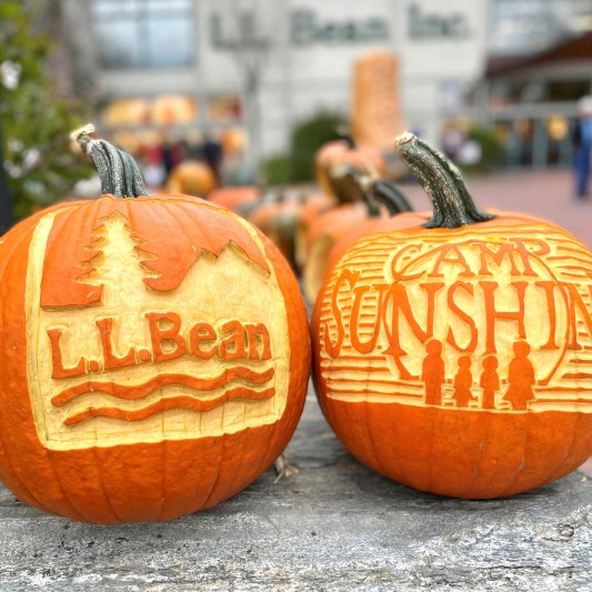 Two hand-carved pumpkins, one with L.L.Bean logo and one with Camp Sunshine logo.