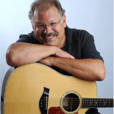 Denny Breau, arms crossed on acoustic guitar in his lap.