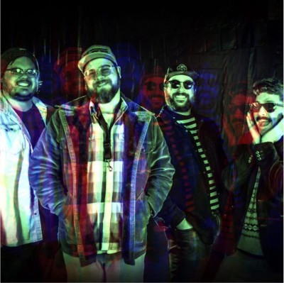 4 members of band "Skosh", dark background, green light on faces.