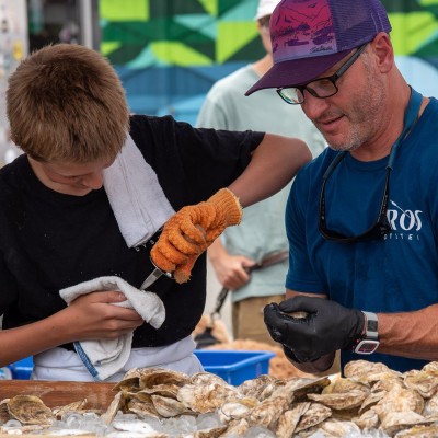 A father and son shucking oysters behind a table covered with oysters on ice.
