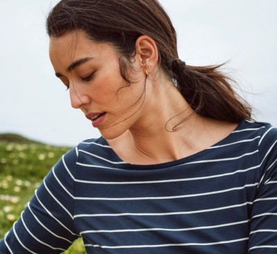 A woman outdoors wearing a navy and white striped shirt with green hills in the distance.