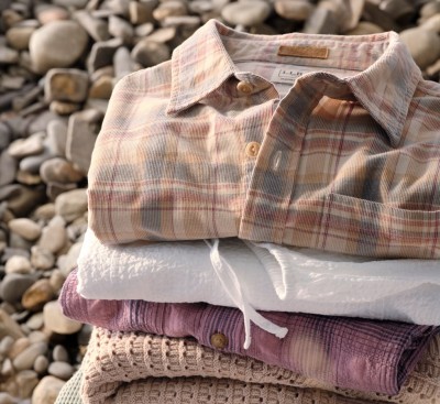 Stack of folded pastel shirts placed on rocks, with soft textures and natural tones in an outdoor setting.