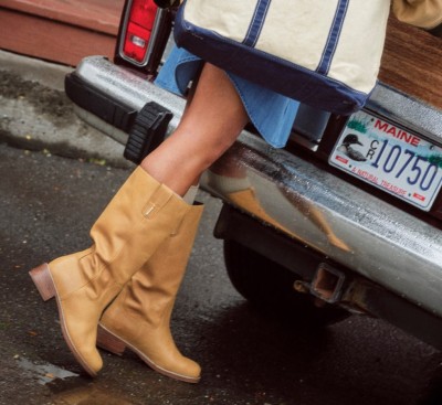 Close-up of tan boots stepping from a vehicle with a Maine license plate on a wet pavement street.