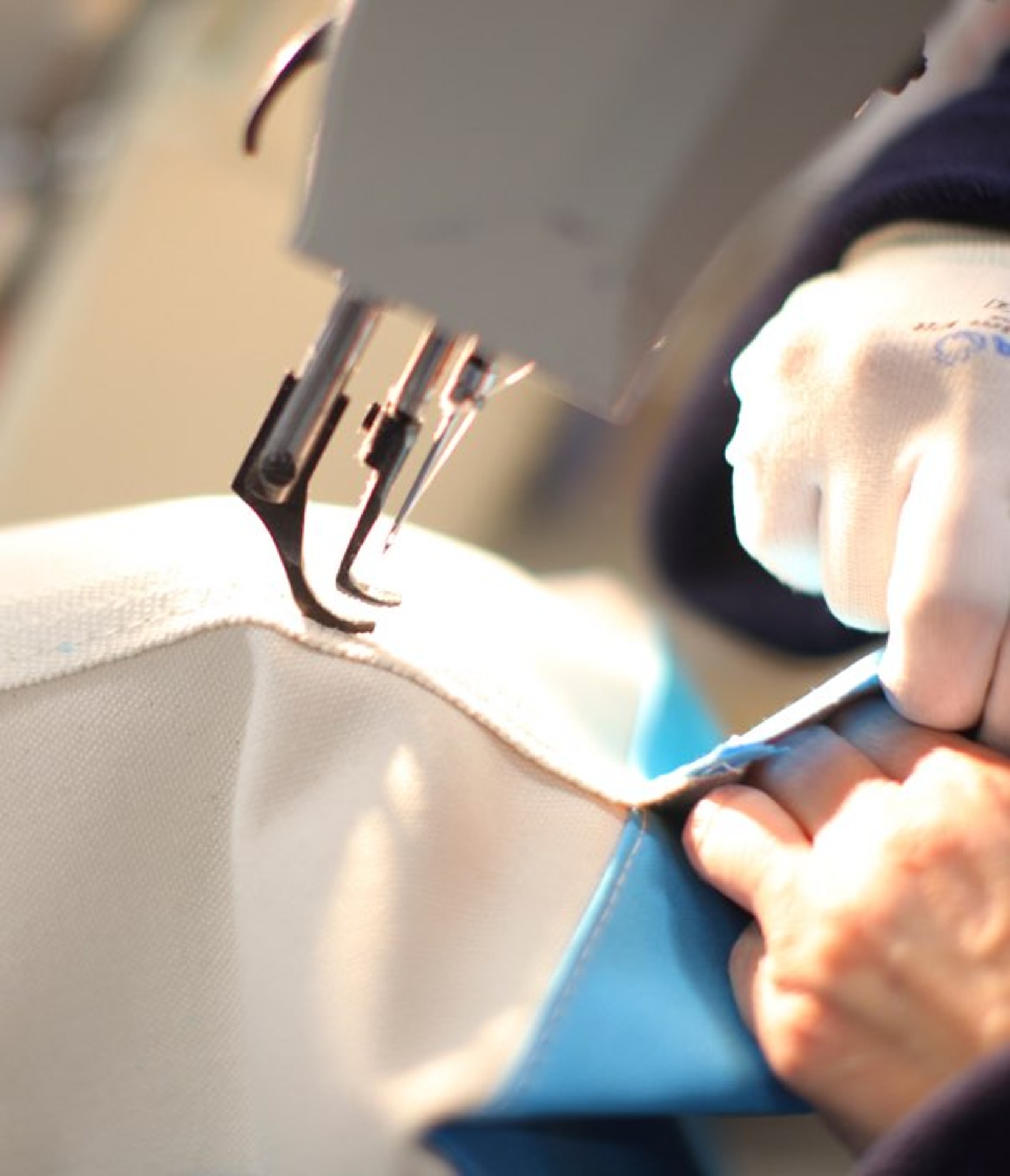 A close-up of a sewing machine stitching canvas fabric as a gloved hand guides the material.