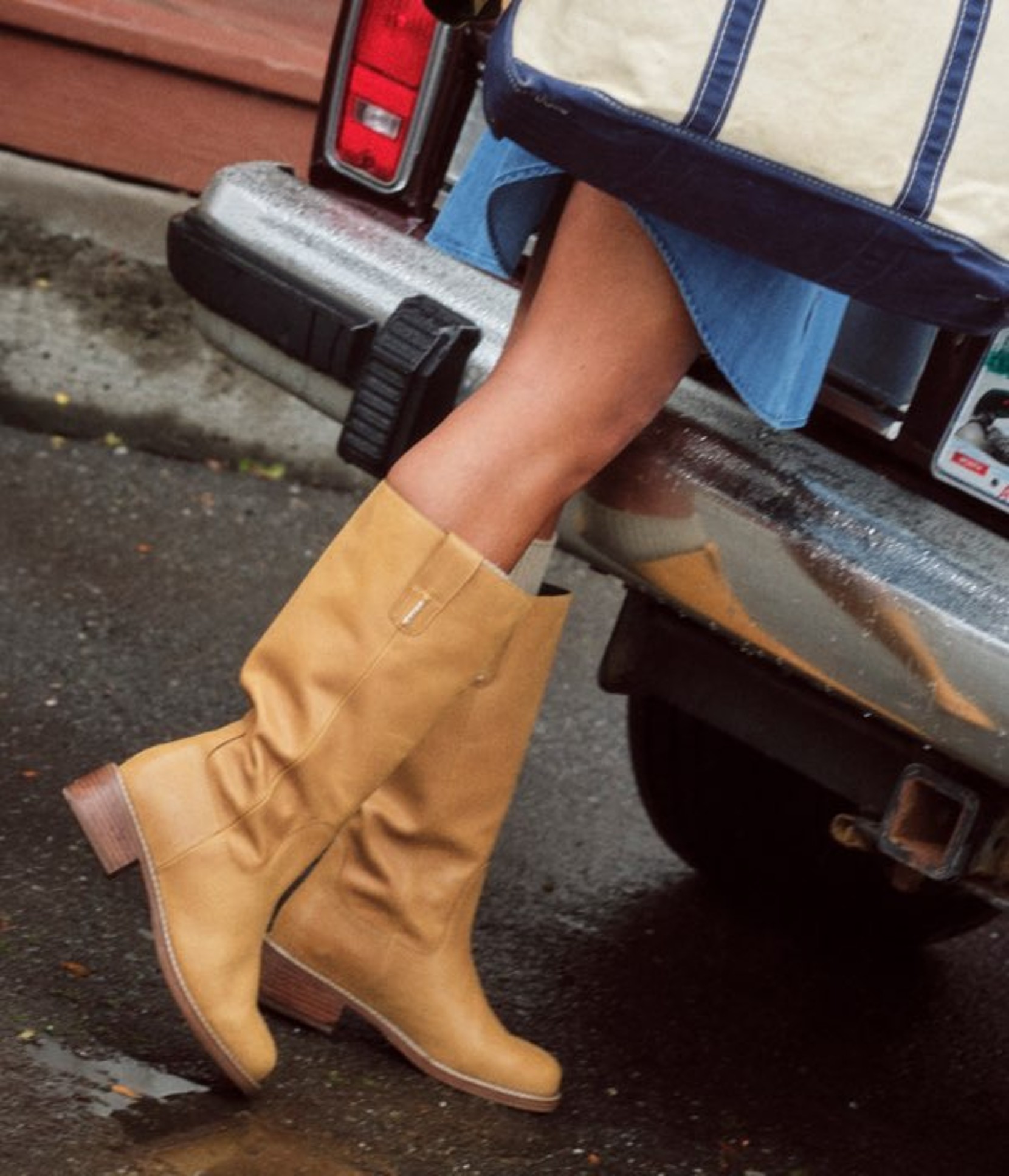 Close-up of tan boots stepping from a vehicle with a Maine license plate on a wet pavement street.