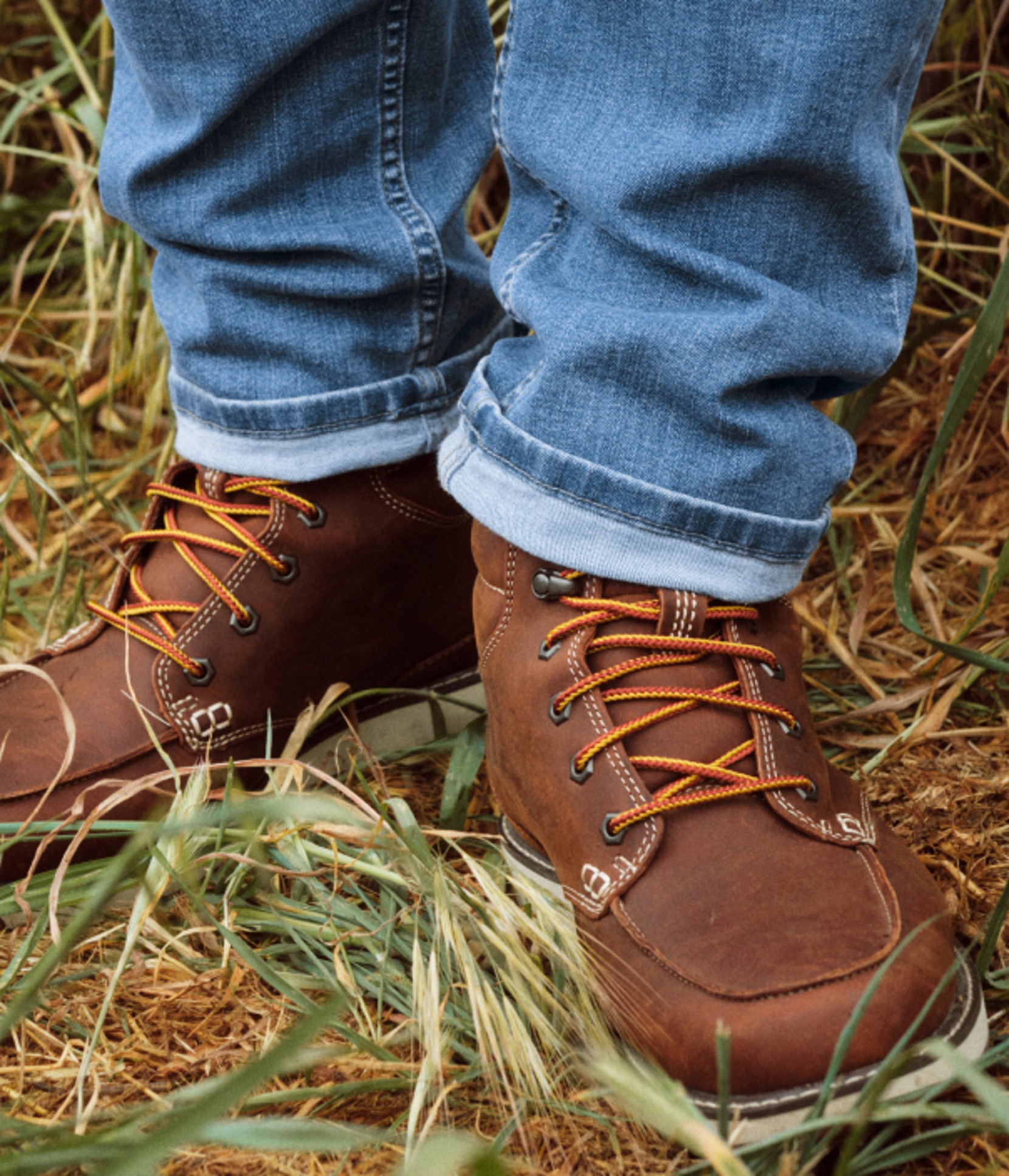 Close-up of brown leather boots and cuffed jeans in grass.