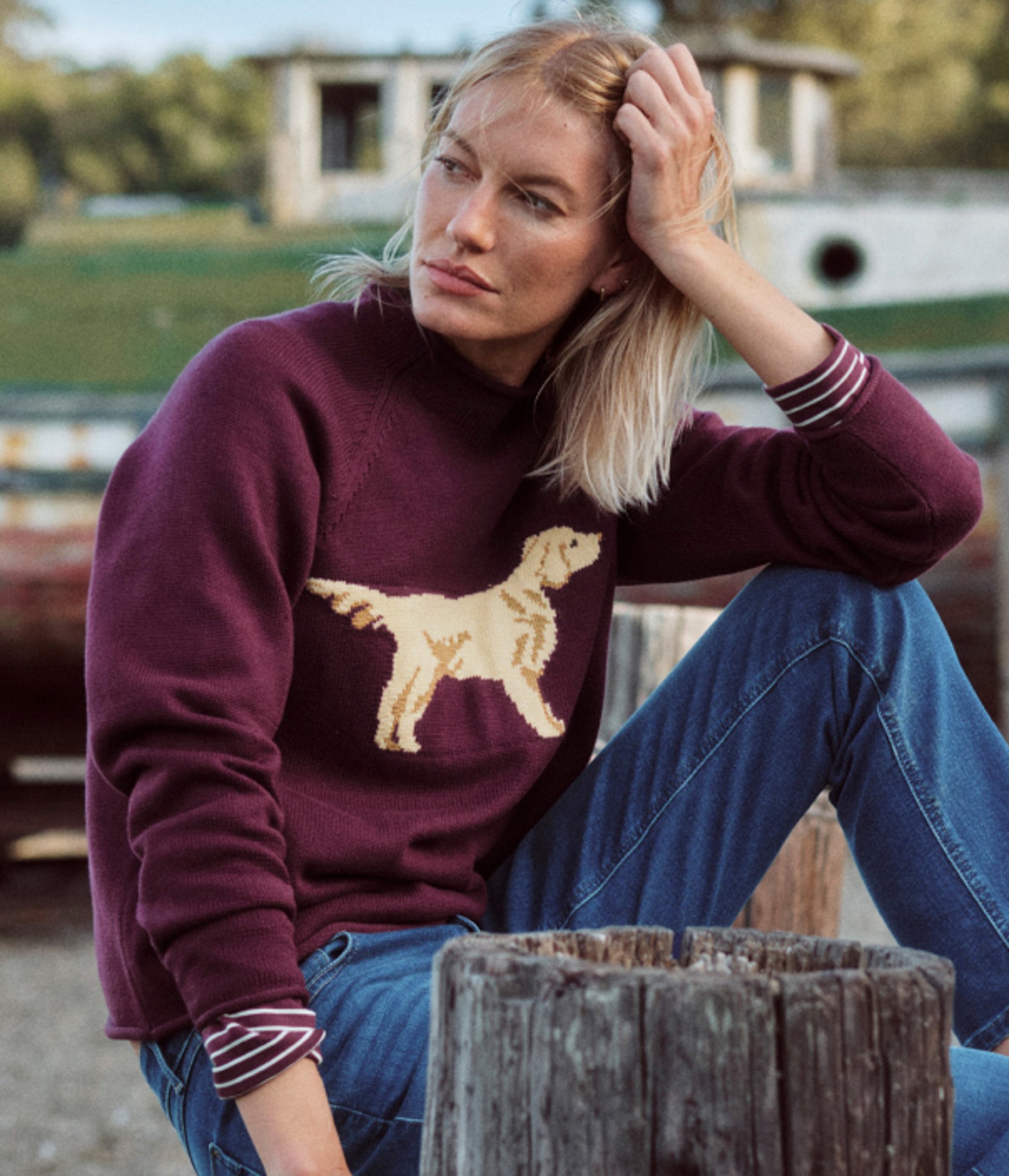 Person in a burgundy sweater with a dog on the front sitting outdoors.