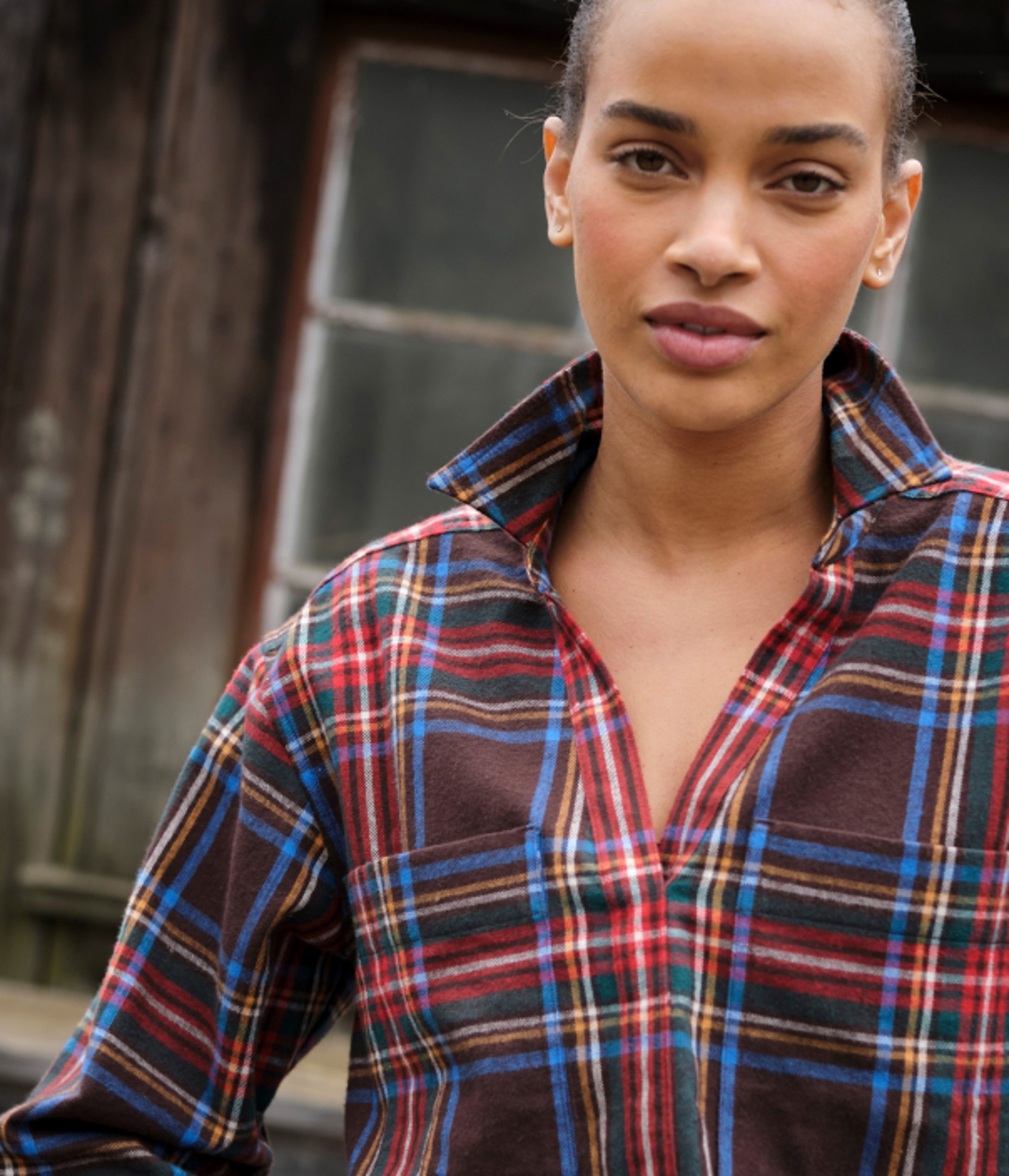 Close-up portrait of a person wearing a brown plaid shirt outdoors.