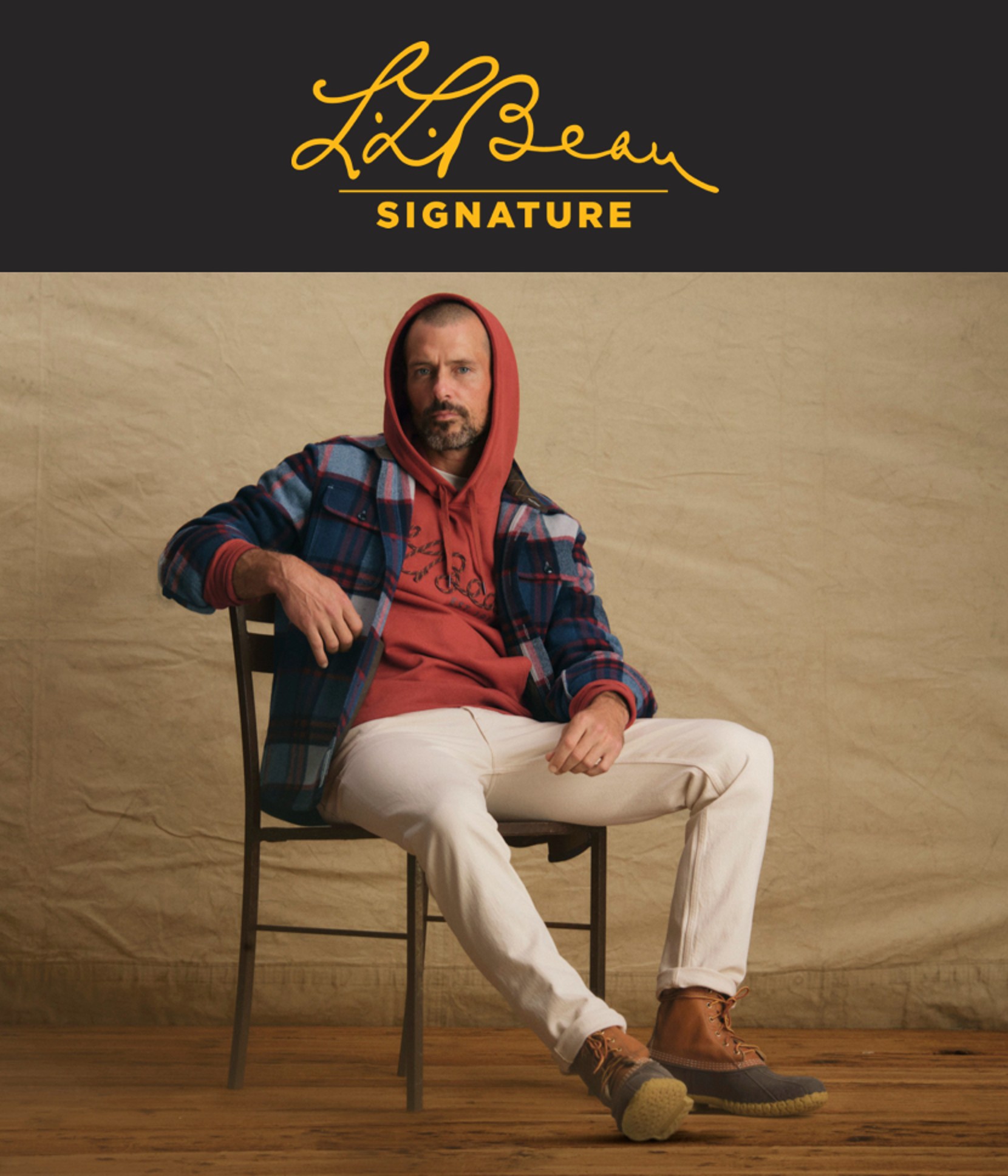 L.L. Bean Signature logo and a man seated, wearing a red hoodie, blue plaid overshirt, white pants, and brown boots.