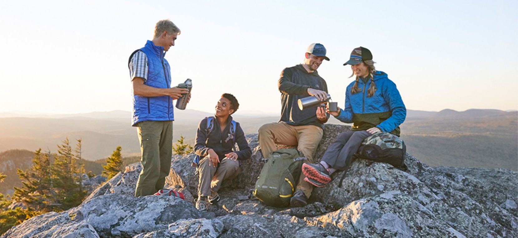 A group of 4 hikers stop for a water break on top of a mountain.