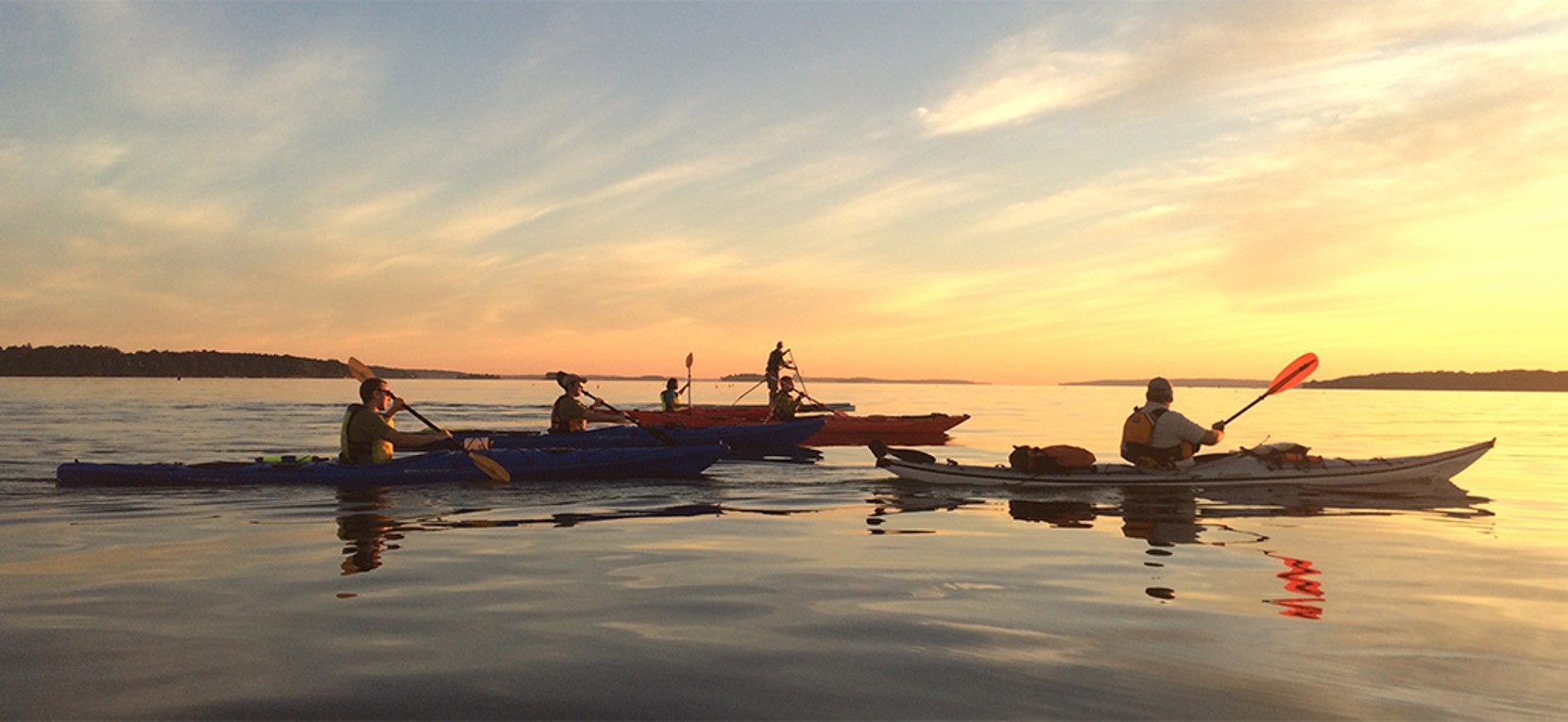 A group of people enjoying a sunset kayak and paddleboard in the ocean. 