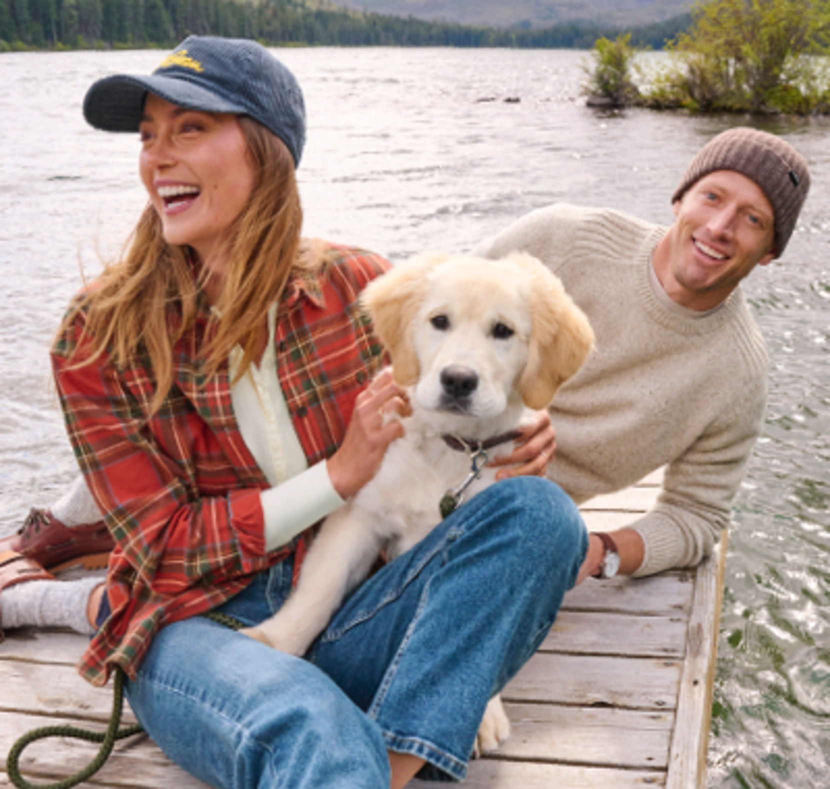 Two people and a dog sitting on a lakeside dock.
